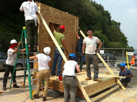 eric is standing on floor panel as other students attach the wall panel to floor